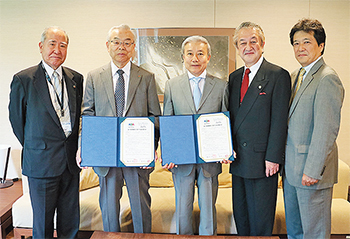 サインを終えた協定書を手にする塩野院長（当時、左から2 番目）と鶴岡会長（その右）