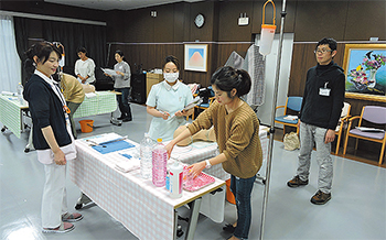 「医療的ケア」の演習で経管栄養について学ぶ受講者。色水を栄養剤に見立て、チューブに着脱するトレーニング